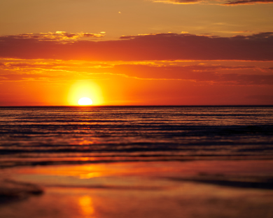 A serene sunset over the ocean, with vibrant orange and yellow hues reflecting on the water's surface. The tranquil scene captures the beauty of nature's evening light and coastal serenity.