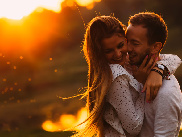 A couple sharing a joyful moment together during sunset, surrounded by a beautiful natural landscape with warm, golden light illuminating their faces.